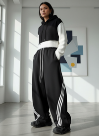 Person wearing a black tracksuit with white stripes in a modern room.